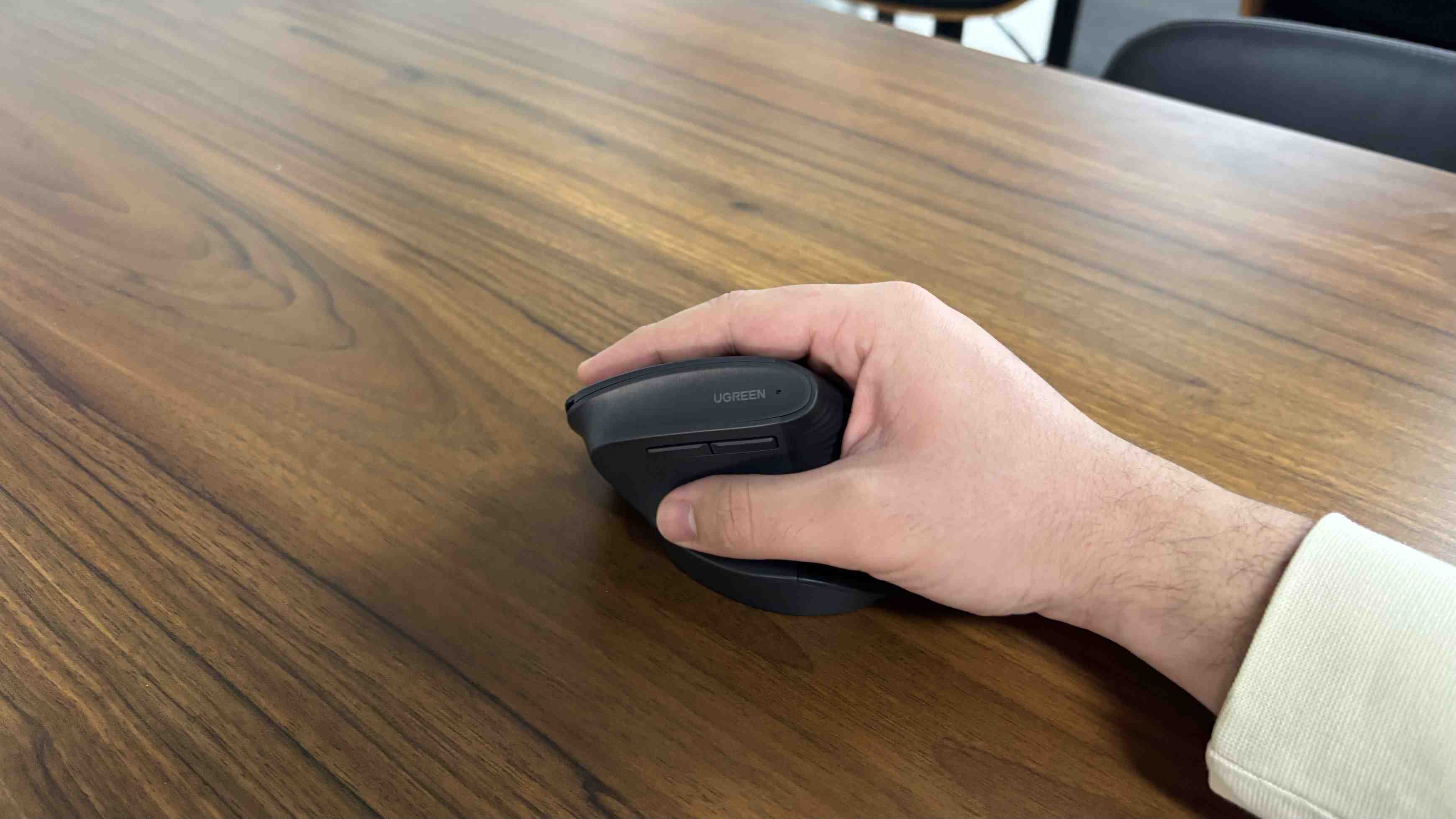 A hand grips the upright Ugreen mouse on a wooden tabletop.